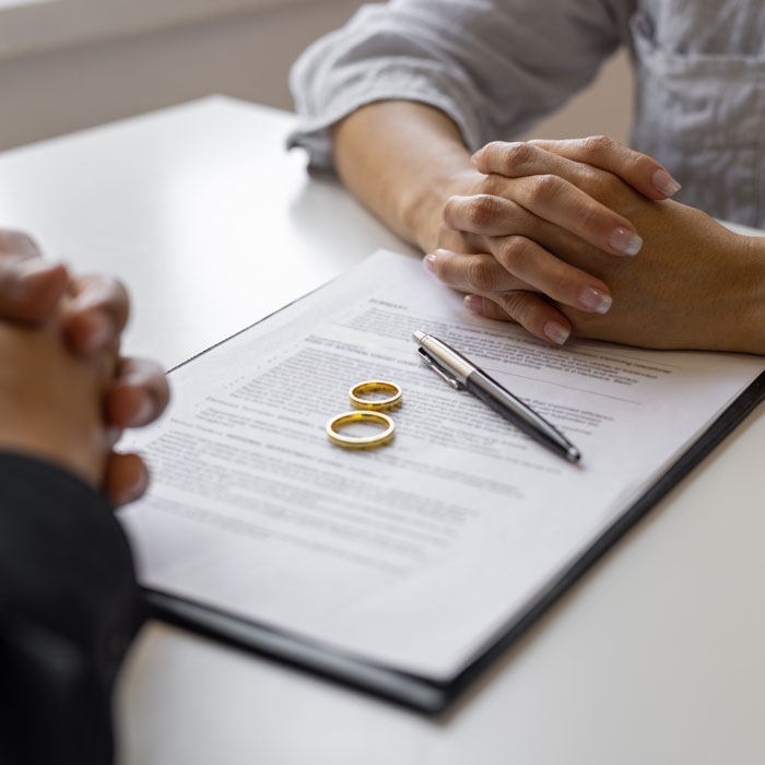 couple with their hands clasped across the table from each other with document and wedding rings between them